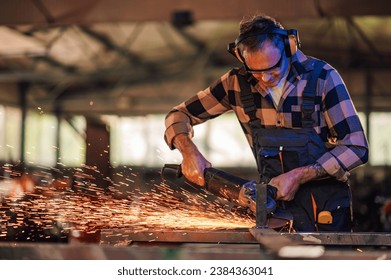 Young expert in the workshop carefully grinding metal while shaping it to perfection and creating sturdy structures of the construction. Dedicated work in a dangerous environment. Wearing safety gear. - Powered by Shutterstock