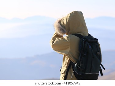 young Explorer with Backpack admires the view from the top of a mountain in winter