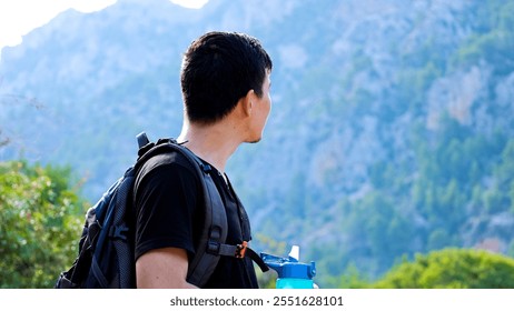 Young explorer man with backpack looking at mountains in the background on a sunny day