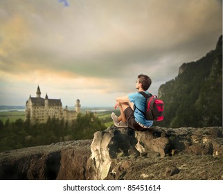 Young explorer sitting on a rock in front of a fairy tale castle - Powered by Shutterstock