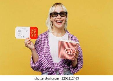Young expressive blonde smiling cheerful happy satisfied woman in 3d glasses watch movie film hold bucket of popcorn in cinema ticket laughing isolated on plain yellow color background studio portrait