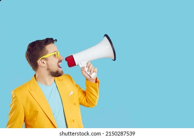 Young expressive man using megaphone announces discounts and sales on light blue background. Man makes loud announcement near copy space. Concept of marketing, summer sales and discounts.