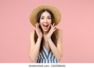 Young expressive woman 20s wearing summer clothes striped dress straw hat scream shout news with hands near mouth isolated on pastel pink color background studio portrait. People lifestyle concept.