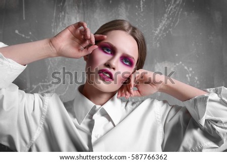 Young extravagant model with bright makeup near grunge wall