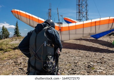A young extremal guy preparing and double-checking his special equipment and gears for a Hang gliding fly. View from the behind