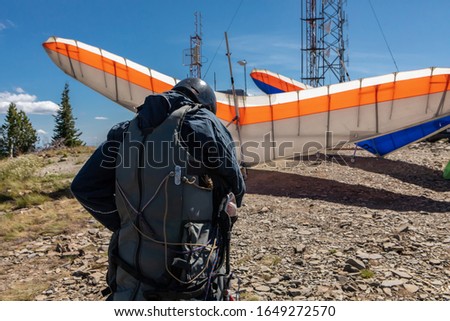 A young extremal guy preparing and double-checking his special equipment and gears for a Hang gliding fly. View from the behind