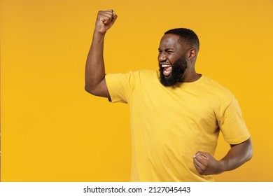 Young exultant happy black man 20s in bright casual t-shirt doing winner gesture celebrate clenching fists say yes isolated on plain yellow color background studio portrait. People lifestyle concept - Shutterstock ID 2127045443