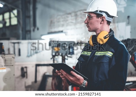 Young factory worker using adept tablet computer in a workshop building . Industrial technology and manufacturing software configuration .