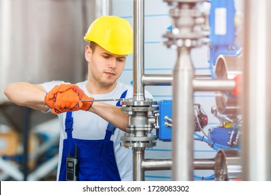 A young factory worker in a yellow hard hat tightens the nut with a wrench on the connection of stainless steel pipes. Installation of complex equipment for industrial water purification. - Powered by Shutterstock