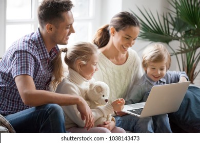 Young Family With Adopted Children Using Laptop Together At Home, Smiling Parents And Son Daughter Relaxing With Computer Looking At Screen, Married Couple With Kids Shopping Or Watching Video Online