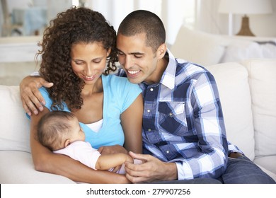 Young Family With Baby Relaxing On Sofa At Home