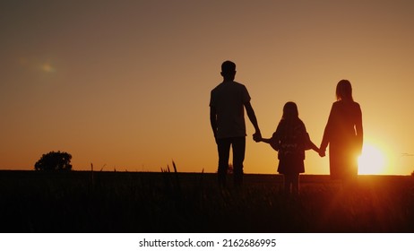Young family with a child admiring the sunset in the field, holding hands - Shutterstock ID 2162686995