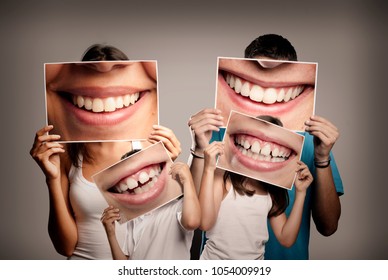 Young Family With Children Holding A Picture Of A Mouth Smiling On A Gray Background