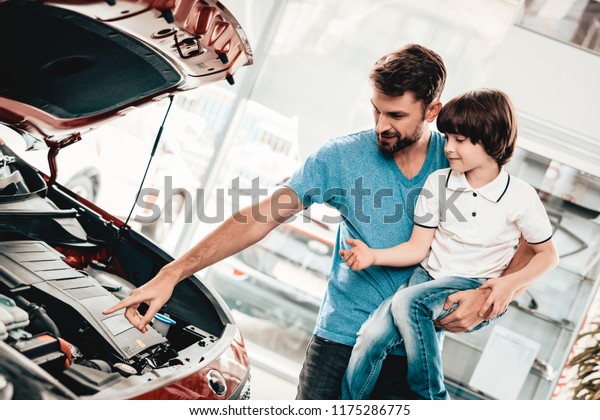 Young Family\
Are Choosing A New Car In Showroom. Automobile Salon. Father And\
Son. Good Mood. Make A Desicion. Auto Rewiew. Quality Control.\
Reliability Mark. Looking Under The\
Hood.