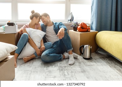 Young family couple bought or rented their first small apartment. They sit on floor very close and enjoy each other company. Moving unpacking. Lovely cheerful couple.