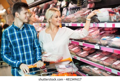 Young family couple choosing chilled meat in food store