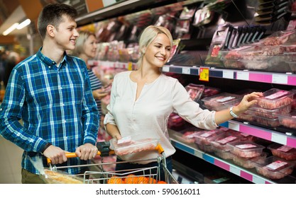 Young family couple choosing chilled meat in food store