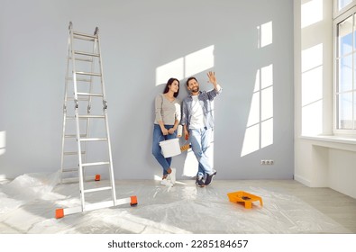 Young family couple doing renovations at home. Happy man and woman painting walls and decorating their house. Husband and wife with bucket and roller standing by wall and discussing interior design - Shutterstock ID 2285184657