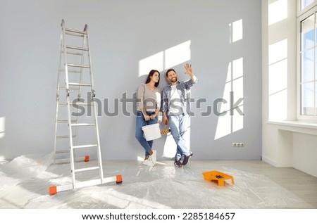 Young family couple doing renovations at home. Happy man and woman painting walls and decorating their house. Husband and wife with bucket and roller standing by wall and discussing interior design
