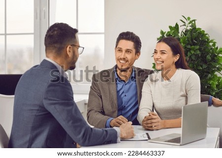 Young family couple meeting with real estate agent or loan broker. Happy, smiling man and woman sitting at office desk with realtor, business advisor or loan manager