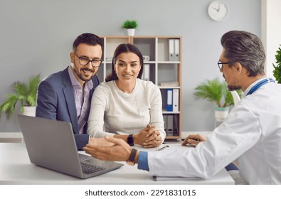 Young family couple planning children and visiting doctor. Doctor talking to happy husband and wife, explaining details of IVF treatment, pointing at laptop computer and showing something on screen - Powered by Shutterstock