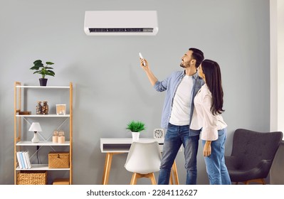 Joven pareja familiar usando su moderno sistema de aire acondicionado en casa. Feliz marido y mujer instalando la temperatura en su aire blanco en la pared de la sala de estar. Concepto de aire acondicionado