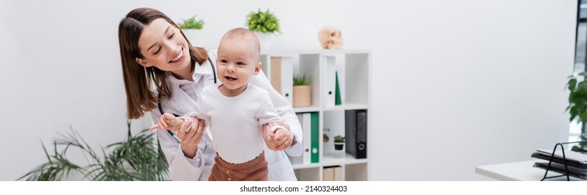 Young family doctor holding hands of baby in hospital, banner - Powered by Shutterstock