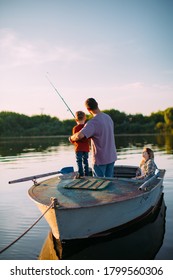 Young Family Fishing On Boat In Summertime. Father Teaches Son Fishing. Back View. Photo For Blog About Family Travel