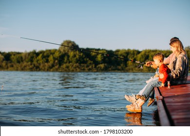 Young Family Fishing On The Pier On The River Or Lake In Summertime. Photography For Ad Or Blog About Family And Travel