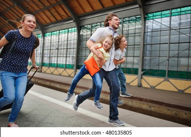 Young Family Of Four Is Late For A Train. Mum Drags Luggage. The Daddy Bears Both Children. Parents Run. Children Laugh.