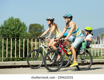 Young family of four people with bikes in sports helmets outdoors