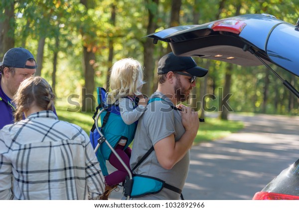 young family getting kid in backpack for a fall\
hike in the woods