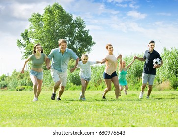 Young Family Happily Playing And Running Together Outdoors On Green Meadow