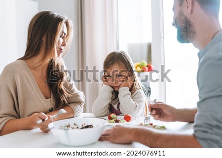 Young family has lunch at table in bright kitchen at home. The daughter does not want to eat and parents are worried