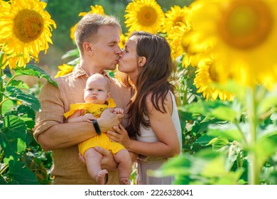 Young Family Having Fun In The Field Of Sunflowers In Summer. Father And Mother Holding Little Baby Daughter. Summer Season, Freedom, Family Value Concept.