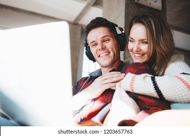 Young family at home. Husband and wife sitting on the couch and watching TV series on laptop and listening music. Bright loft apartment