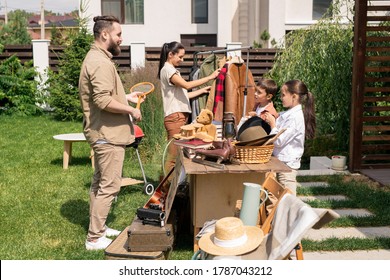 Young Family With Kids Preparing Things For Garage Sale While Clearing House Before Moving