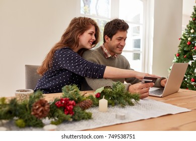 Young Family With Laptop And Credit Card Buying Online Christmas And New Year Gifts. Couple Doing Online Shopping For Christmas.