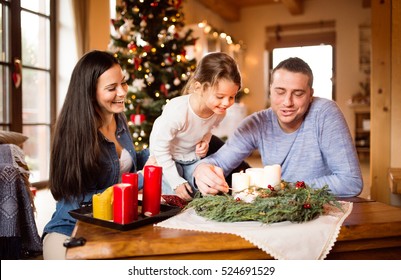 Young Family Lighting Candles On Advent Wreath. Christmas Tree.