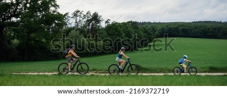 Young family with little child riding bicycles on path in park in summer.