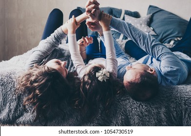 Young family are lying on bed and playing with their hands. Mom, dad and little daughter. People are enjoying their company. Childhood and parenthood. Happiness. Happy moments. Casual lifestyle. 
