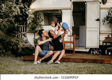 a young family meets the sunset near his mobile home, dad, mom and daughter, a young girl holds her daughter in her arms, her husband sits nearby and hugs his wife, a beautiful family image