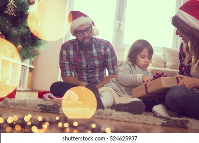 Young Family On Christmas Morning Exchanging Presents And Enjoying Their Time Together. Focus On The Baby Girl