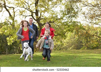 Young Family Outdoors Walking Through Park With Dog