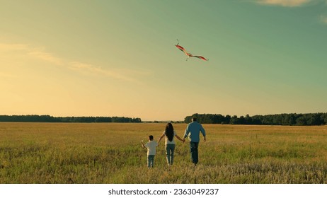 Young family is playing with kite in meadow. Happy family with baby in park playing with kite. Family walk on grass, child dreams of flying. Active people together travel to nature. Kid wants to fly - Powered by Shutterstock