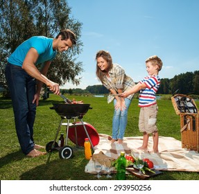 Young Family Preparing Sausages On A Grill Outdoors 