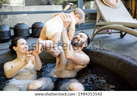 Young family relaxing with a little baby boy at spa, sitting in the hot vat outdoors. Family on vacation with a child