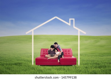 Young Family Seated On A Sofa Dreaming A Home In The Nature