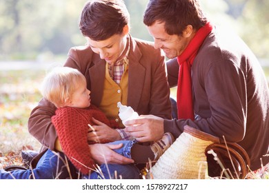 Une jeune famille assise sur l'herbe, le père nourrit le bébé