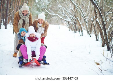 Young Family Sitting On A Sled In The Snow